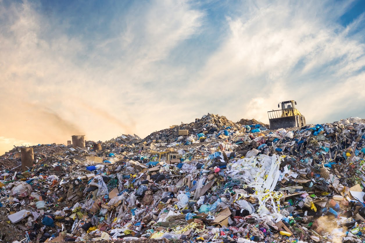 A Massive Garbage Pile In A Landfill, With Construction Machinery In Background.