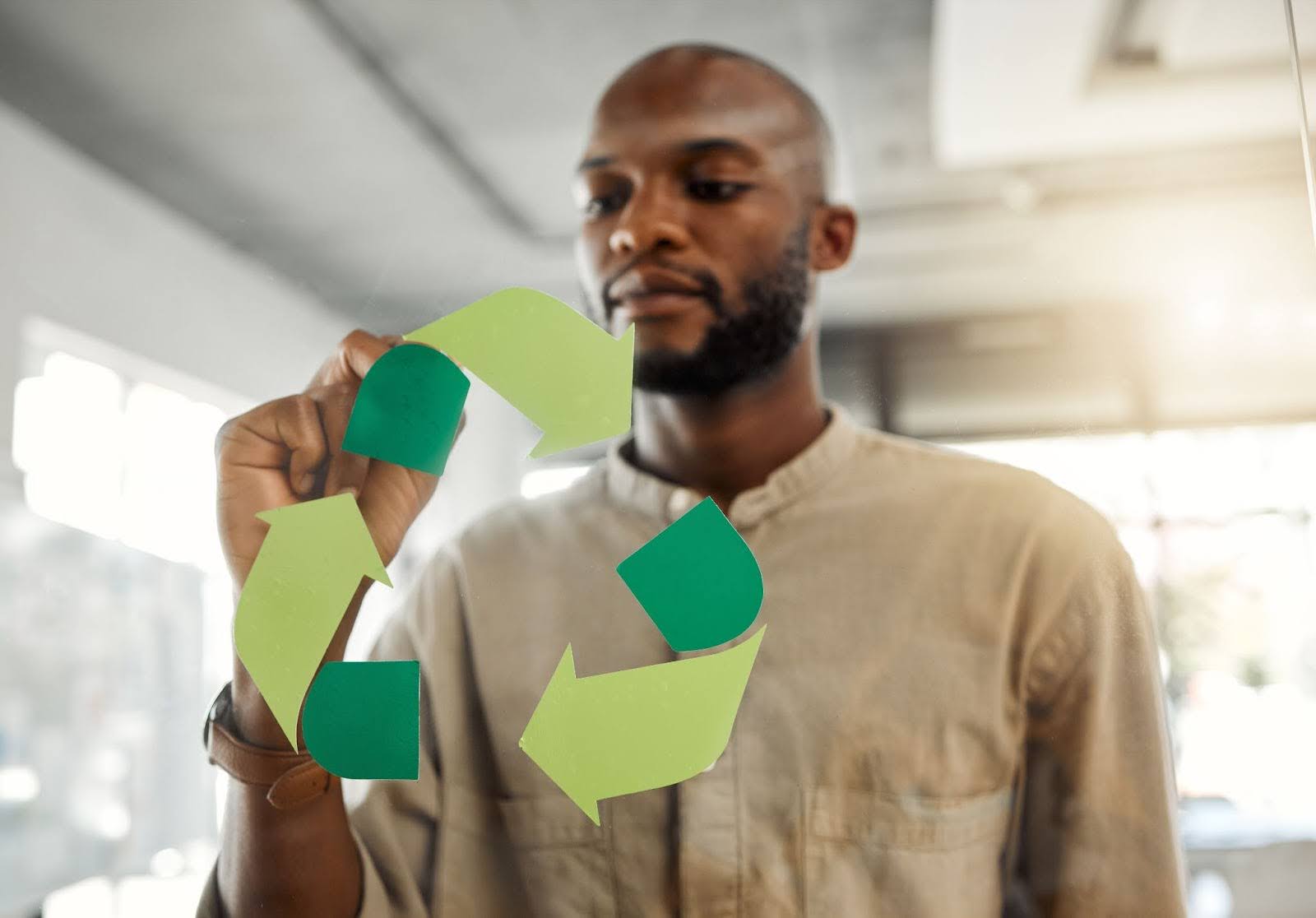 Focused Businessman Drawing A Recycling Symbol On A Glass Window, Representing Corporate Green Programs