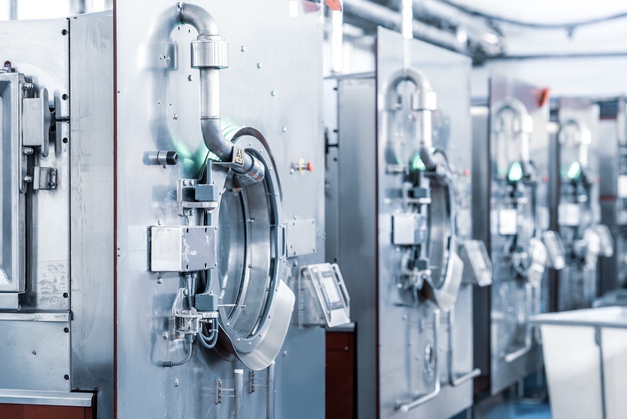 An Image Of A Line Of Shiny Stainless Steel Industrial Washing Machines.