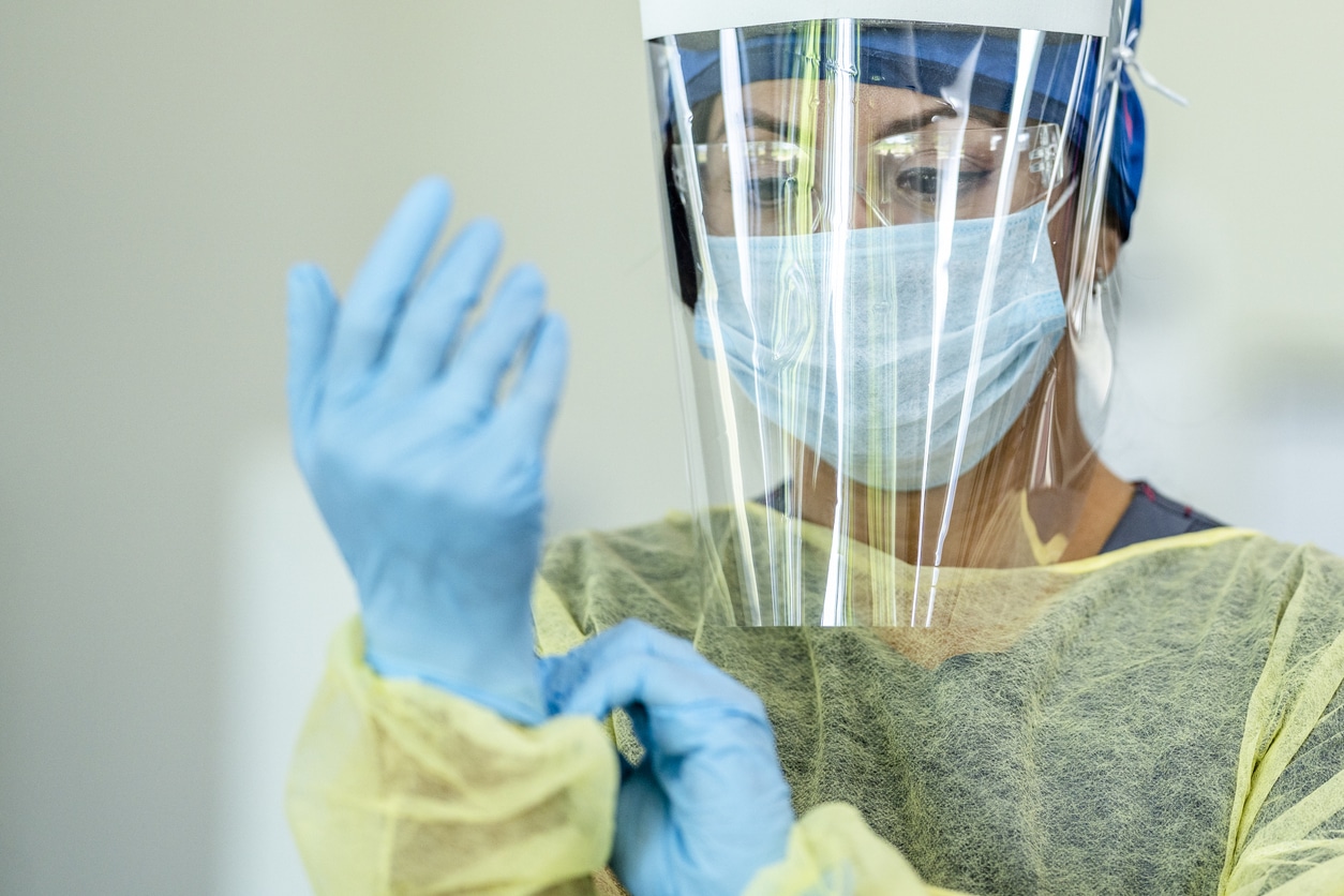 Woman Putting On PPE, Including Gloves, Mask, Face Shield, And Smock.