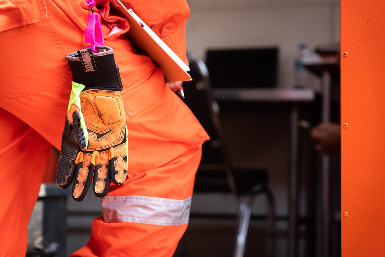 A Safety Orange Impact Glove Hangs From The Toolbelt Of A Worker In A Safety Suit